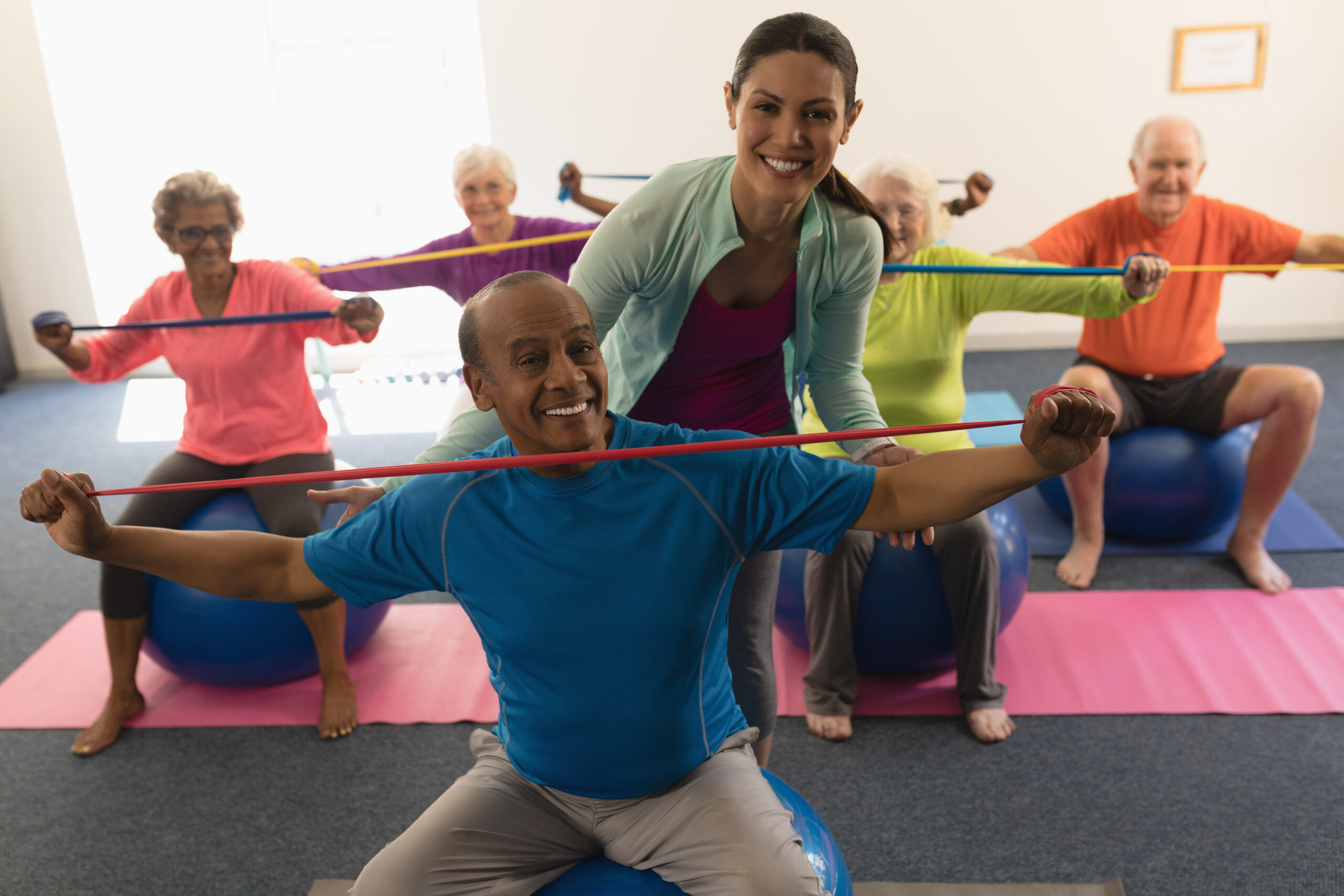 Front view of happy young female trainer assisting senior man in fitness studio